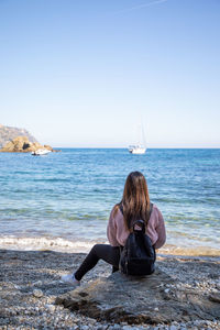 Rear view of woman sitting at beach against clear sky