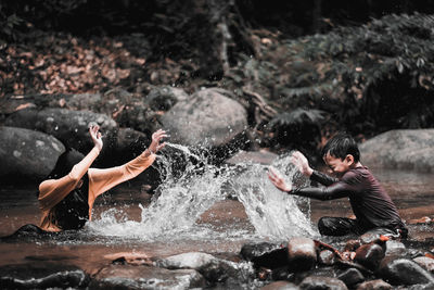 Cheerful siblings splashing water in river