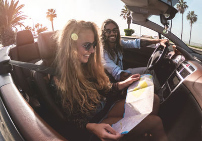 Happy friends looking at map while sitting in car