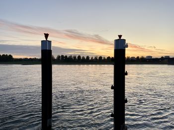 Silhouette wooden post in sea against sky during sunset