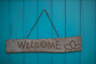 Close-up of welcome sign hanging on turquoise door