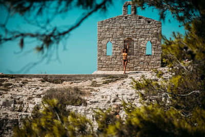 Young woman standing in bikini against stone wall