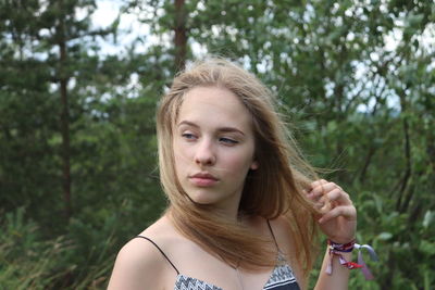 Thoughtful beautiful young woman standing against trees in forest