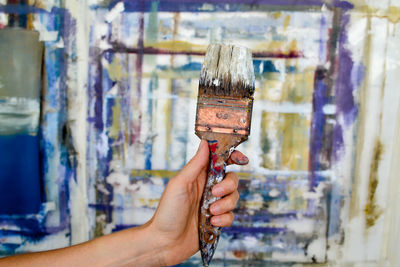 Cropped hand holding paintbrush against wall