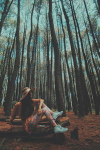 Woman sitting by tree trunk in forest