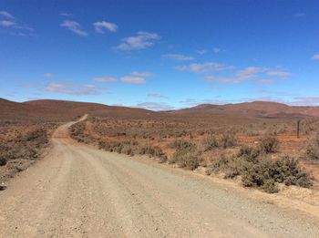 Dirt road amidst desert against sky