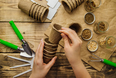 Women's hands hold peat pots. top view of seeds and garden tools on a wooden background.