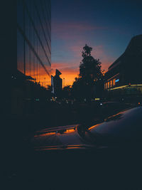 Cars on city street against sky at sunset