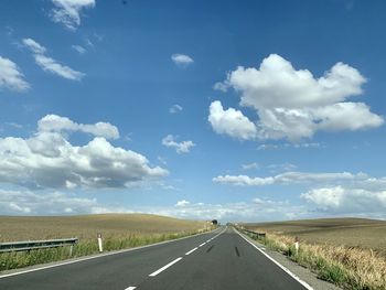 Empty road amidst field against sky