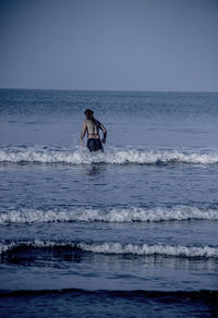 Rear view of shirtless man standing in sea against clear sky