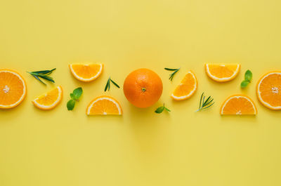 Orange fruits with mint and rosemary leaves on yellow background. summer background concept.