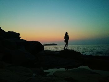 Silhouette woman standing on rock at beach against clear sky