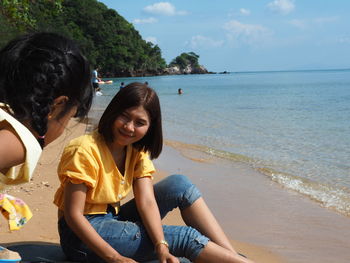 Young woman sitting on beach against sea