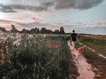 Rear view of dog and woman walking on field