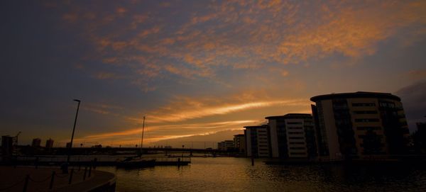 Buildings by sea against sky during sunset