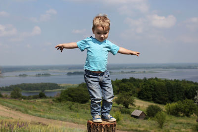 Full length of boy standing on tree trunk against landscape