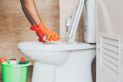 Cropped hands of person cleaning toilet bowl with brush