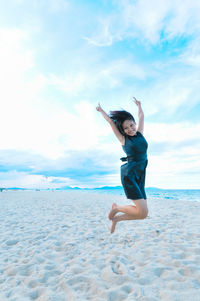 Portrait of young woman jumping at beach against sky