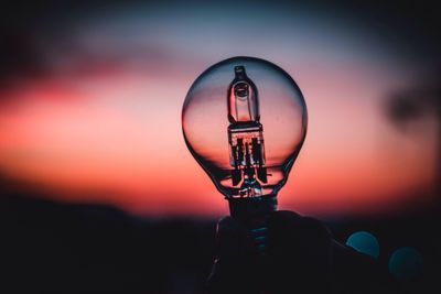 Cropped hand of person holding light bulb against sky