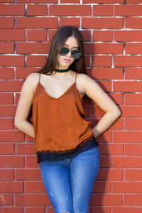 Young woman wearing sunglasses standing against brick wall