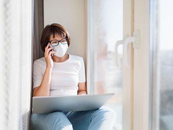 Woman in medical mask remote works from home with smartphone and laptop. quarantine coronavirus.