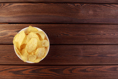 Cheese and chive potato crisp snack in brown bowl on wooden background top view