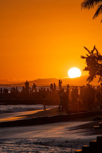 Silhouette people on beach against orange sky