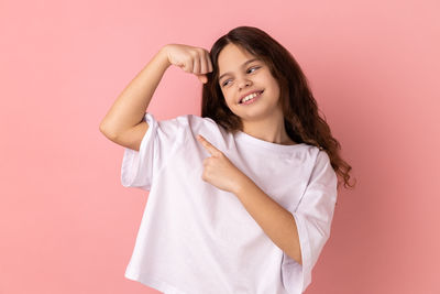 Portrait of young woman standing against pink background