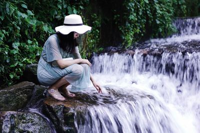 Woman crouching on rock at waterfall in forest