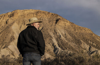 Adult man in cowboy hat standing against mountains in tabernas desert. almeria, spain