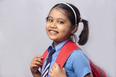 Portrait of a happy smiling indian girl child student in blue school uniform with red bag