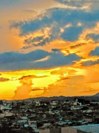 Buildings in city against dramatic sky during sunset