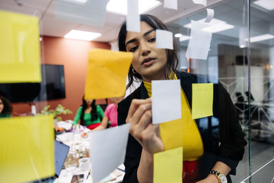 Businesswoman writing on adhesive note during brainstorming session at office