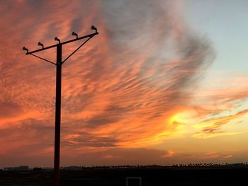 Low angle view of silhouette telephone pole against dramatic sky during sunset