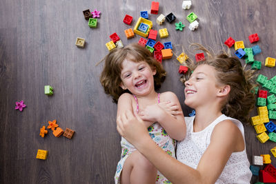 High angle view of happy siblings playing amidst toy blocks on parquet floor