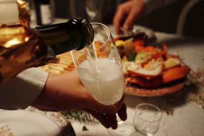 Cropped hand pouring champagne in flute from bottle over table