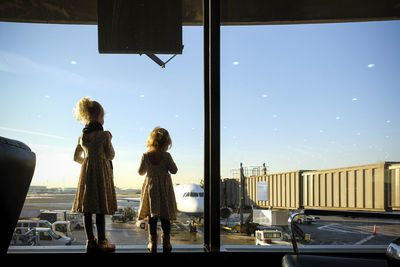 Rear view of sisters looking through window while standing at airport