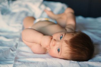Portrait of cute baby with blue eyes lying on bed at home