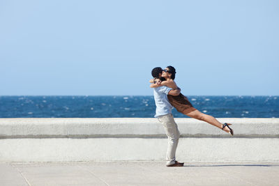 Side view of couple embracing against sky