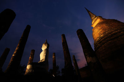 Low angle view of buddha statue and temple against sky at night