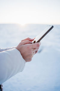 Cropped image of man holding using smart phone snow covered land