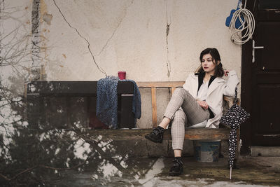 Woman sitting on chair against wall