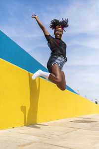 Portrait of cheerful young woman jumping against wall