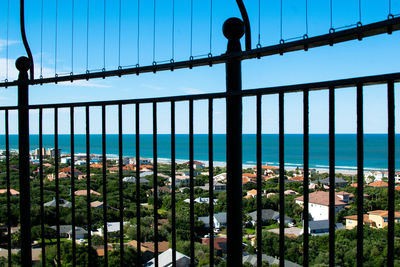 Plants by sea against sky seen through fence