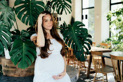Nice young redhead pregnant woman in stylish interior with tropical monsters. 