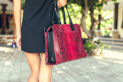 Midsection of woman with red umbrella walking on footpath