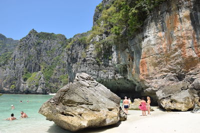 Rear view of people standing on cliff by sea against clear sky