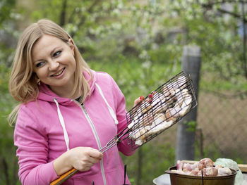 Smiling woman preparing food on barbecue outdoors