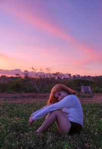 Woman sitting on field during sunset