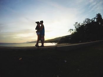Full length of couple kissing at beach against sky during sunset